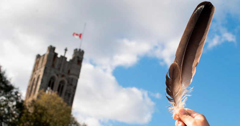feather held up to the sky with University College tower in the background