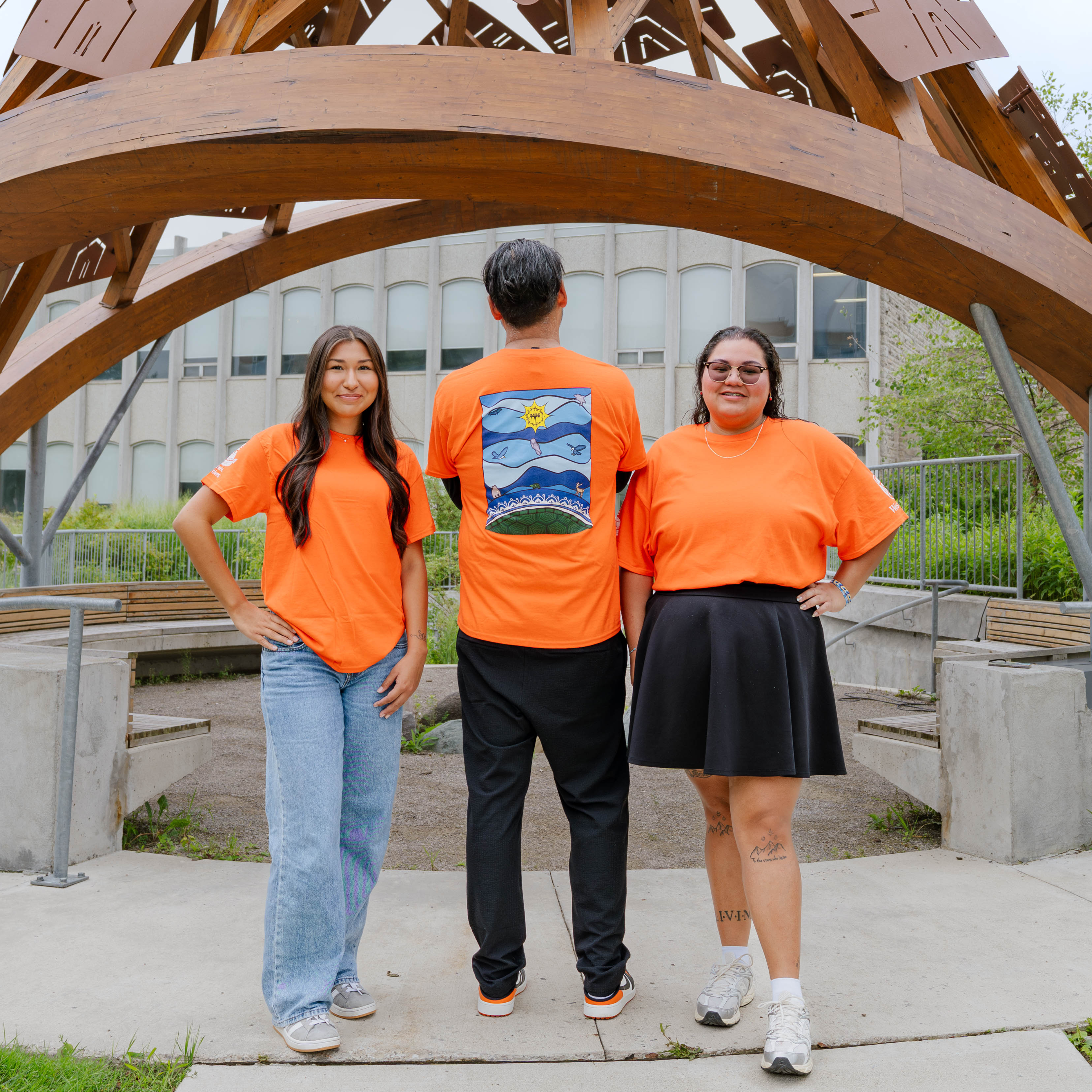 3 people standing together wearing orange shirts, one standing backwards to show a blue design