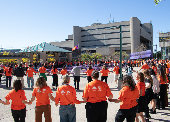 people gathered in a circle holding hands and wearing orange shirts