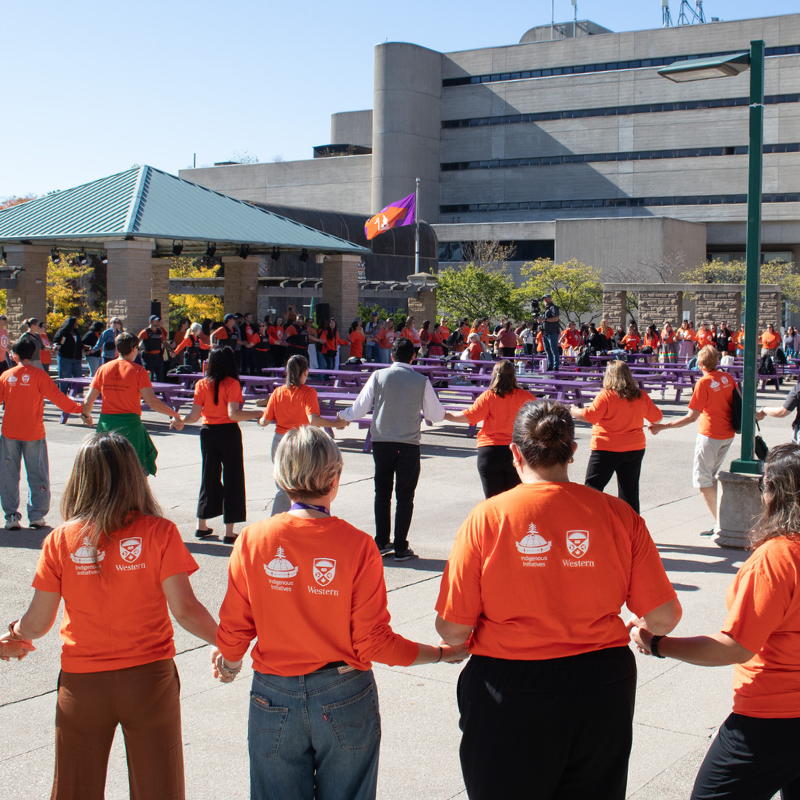 people wear orange shirts and holding hands in a circle